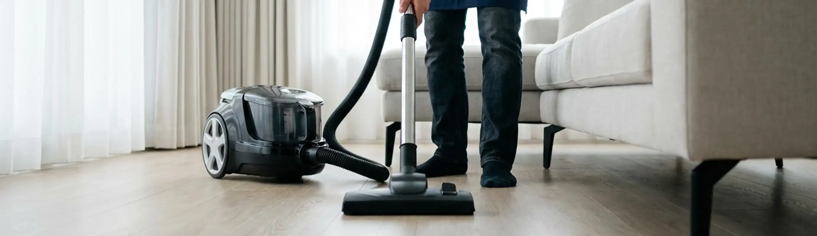 Professional house cleaner vacuuming a living room floor with a canister vacuum cleaner, Fort Lauderdale, FL.