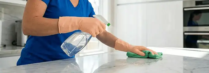 Maid service worker spraying and wiping a kitchen countertop with a microfiber cloth for sanitizing, Fort Lauderdale, FL.