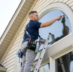 Professional window cleaner on a ladder using a squeegee to clean an exterior arched window, Fort Lauderdale, FL.