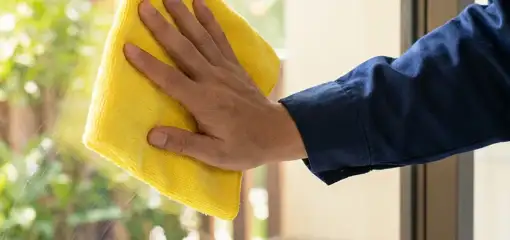 House cleaner wiping a glass window with a yellow microfiber cloth for streak-free cleaning, Fort Lauderdale, FL.